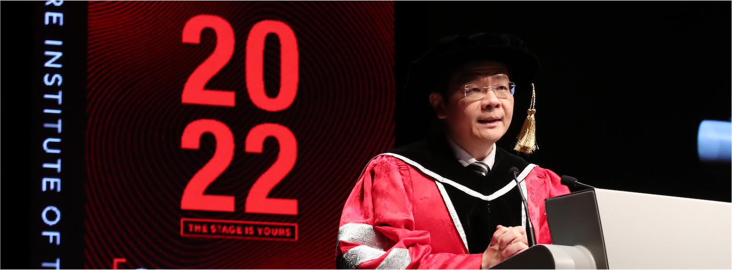 Man in graduation gown at podium next to screen with "2022" and "Institute Of..." text.